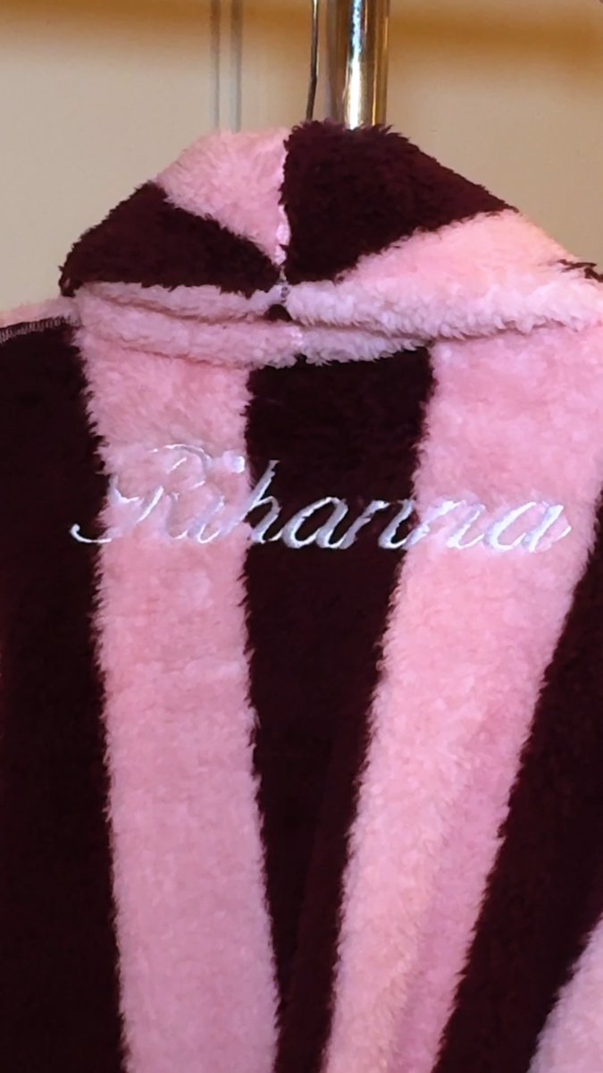 A close-up shows a fluffy pink and dark brown striped robe hanging on a rack with "Rihanna" embroidered in white cursive lettering.