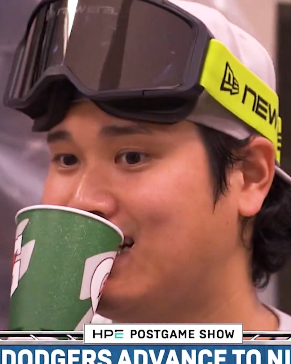 Shohei Ohtani sips from his green paper cup during the "HPE Postgame Show" with a "Dodgers Advance to NL" banner below, celebrating his team's playoff victory while keeping his iconic cup close by.