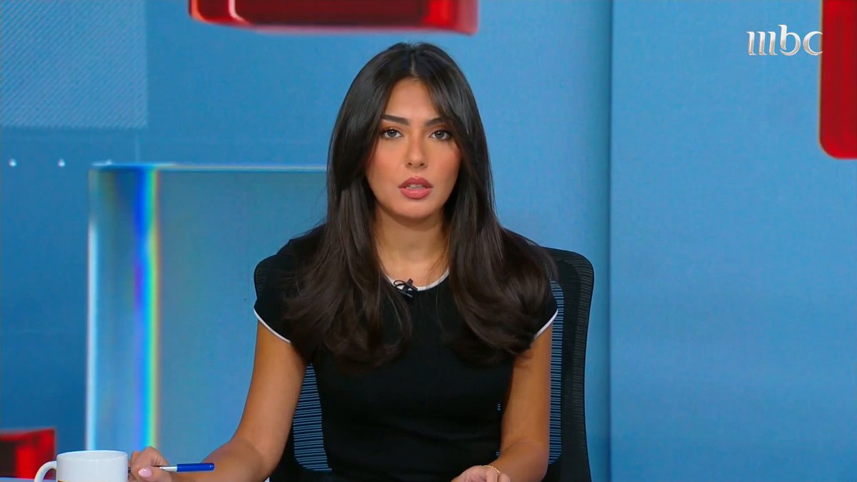 A female MBC1 news presenter sits at a studio desk with a white mug and blue pen, facing the camera against a blue set with red accents. The white “mbc” logo appears in the top-right corner, and the broadcast is shown in the context of a sports update about Al-Fateh ending its relationship with Khaled Al-Otaibi and signing Moroccan coach Jamal Al-Salami, under the hashtag “#نشرة_التاسعة#MBC1”.