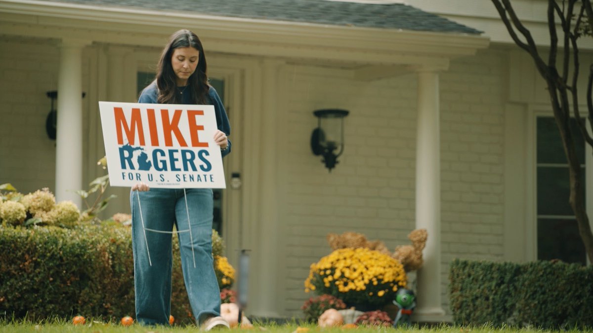 A woman stands in front of a brick house holding a "MIKE ROGERS FOR U.S. SENATE" campaign sign featuring a Michigan silhouette, with fall decorations like pumpkins and mums around the yard. The post's "this is interesting" caption seems to highlight the nostalgic, autumnal political yard-sign scene.