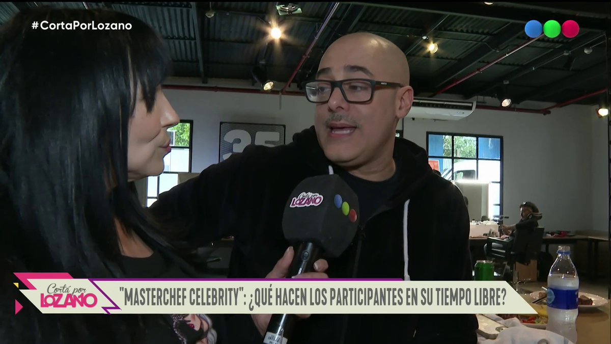A television interview segment from 'Corta por Lozano' with the banner text '"MASTERCHEF CELEBRITY": ¿QUÉ HACEN LOS PARTICIPANTES EN SU TIEMPO LIBRE?' showing a bald man with glasses being interviewed by a woman holding a branded microphone.