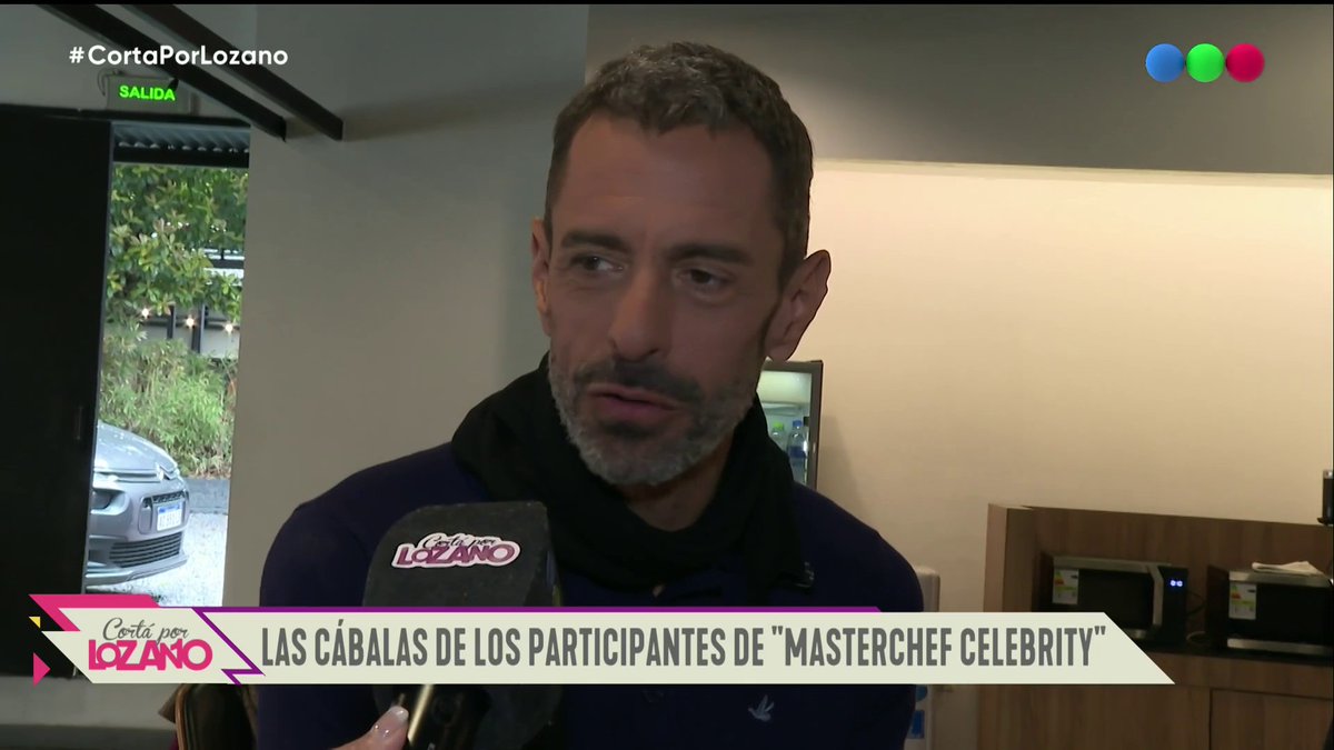 A video screenshot from 'Corta por Lozano' showing a bearded man in a black scarf being interviewed, with the hashtag '#CortaPorLozano' and a chyron reading 'LAS CÁBALAS DE LOS PARTICIPANTES DE "MASTERCHEF CELEBRITY"'.