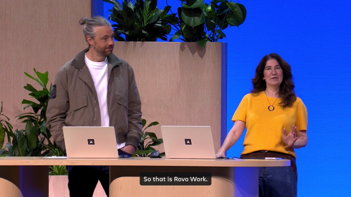Two presenters stand on a stage with laptops displaying the Atlassian logo, with on-screen text reading 'So that is Rovo Work.'