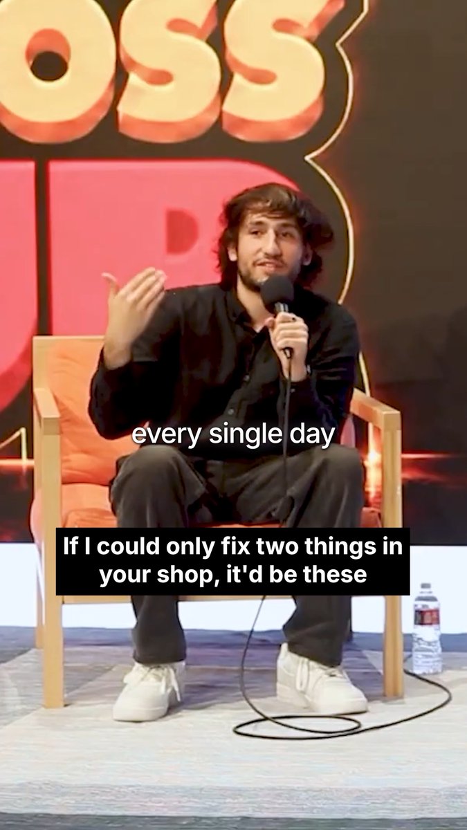 A young man in a black shirt sits in a chair holding a microphone on a stage with a pink 'BOSS' backdrop, with text overlay reading 'every single day' and 'If I could only fix two things in your shop, it'd be these'.