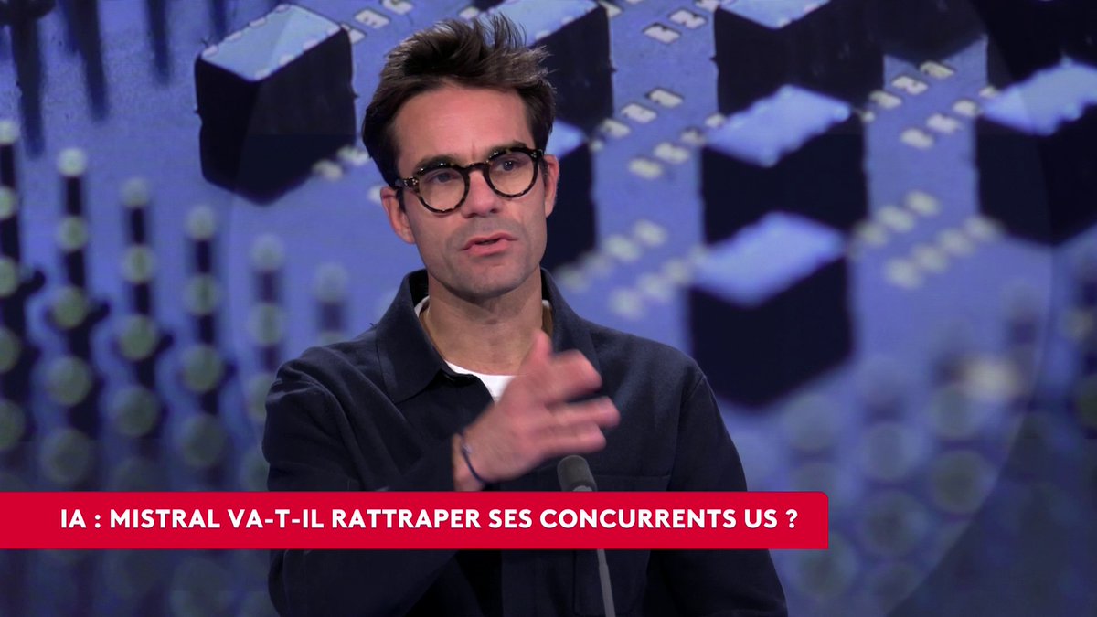 A man wearing round black glasses and a dark jacket speaks into a microphone on a stage, gesturing with one hand. A red lower-third banner reads “IA : MISTRAL VA-T-IL RATTRAPER SES CONCURRENTS US ?,” matching the post about whether Mistral can catch up with international competitors.