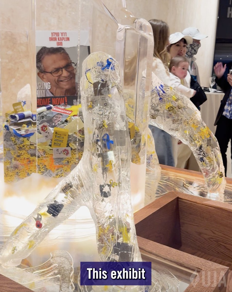 A glass sculpture exhibit features a transparent figure containing yellow ribbons and small notes, alongside a poster reading 'BRING HIM HOME NOW!' with Hebrew text 'דורון קאפלן (60)' identifying the kidnapped person as Doron Kaplan.