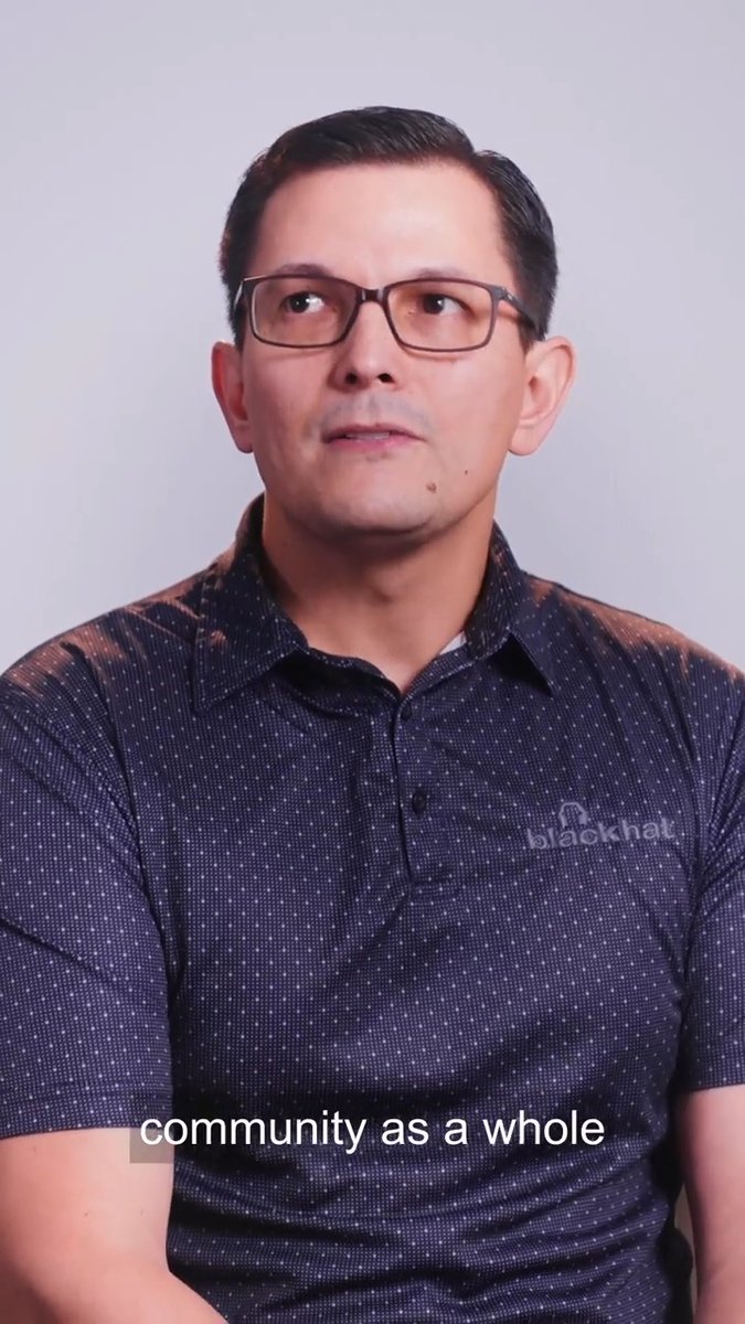 A man wearing glasses and a dark dotted polo shirt sits in front of a light gray background, looking off-camera, with the caption 'community as a whole' at the bottom.
