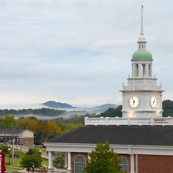 University of the Cumberlands, Boswell Campus Center clock and steeple stands against a cloudy fall sky with foggy mountains in the background.