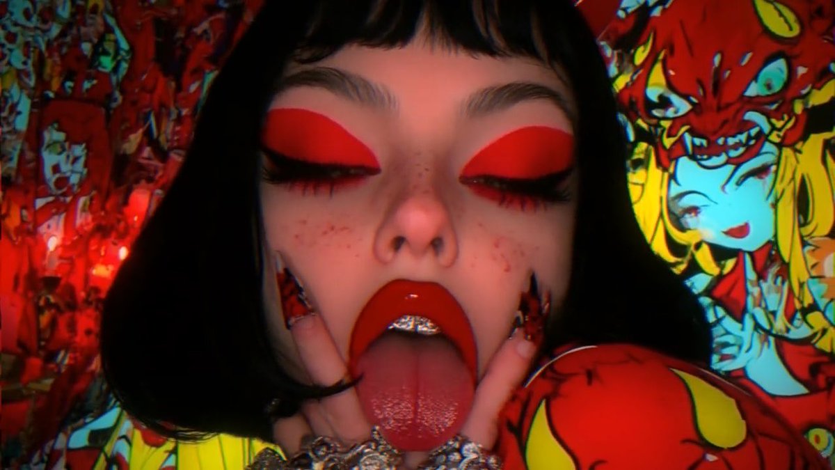 A close-up of a woman with bold red eyeshadow, freckles, and a red tongue out, adorned with ornate silver grills and jewelry, set against a vibrant, chaotic red background featuring cartoonish anime-style demon characters—evoking the lurid, hyper-saturated aesthetic tied to the tweet's "Say My Name Then Disappear" caption.