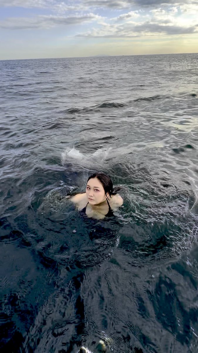 A woman swims in the open ocean at sunset, her head and shoulders visible above the rippling water.
