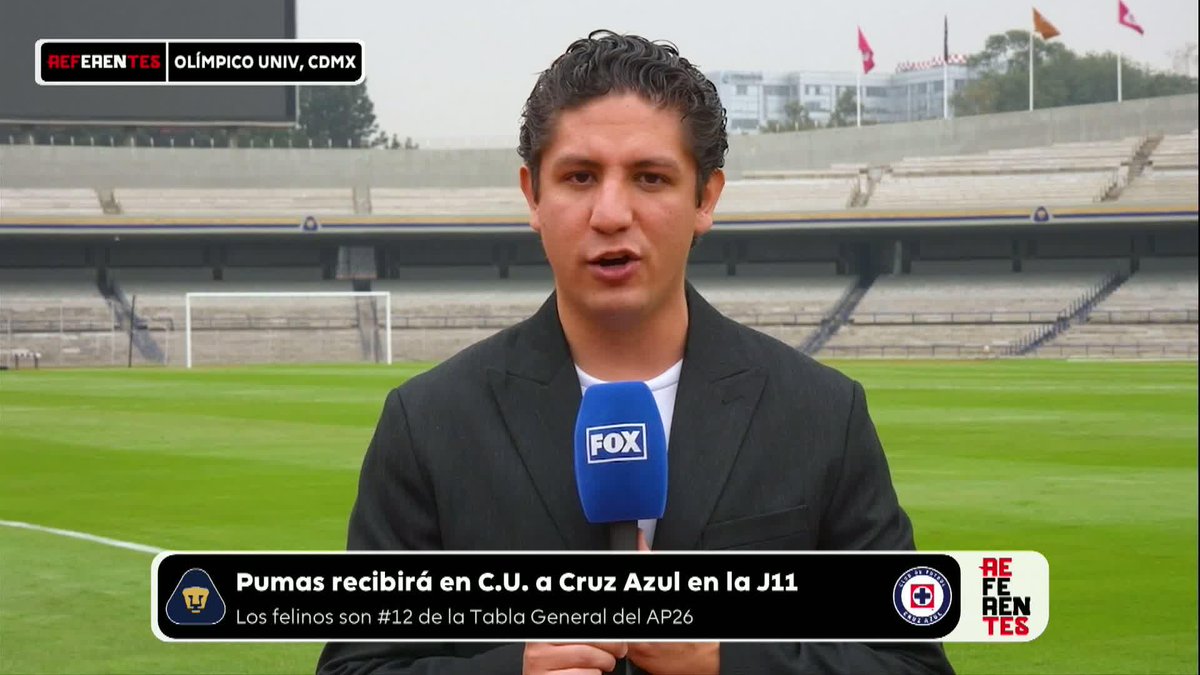 A Fox Sports reporter stands in a stadium with a FOX microphone, with on-screen text reading 'REFERENTES OLÍMPICO UNIV, CDMX' and 'Pumas recibirá en C.U. a Cruz Azul en la J11 - Los felinos son #12 de la Tabla General del AP26'.