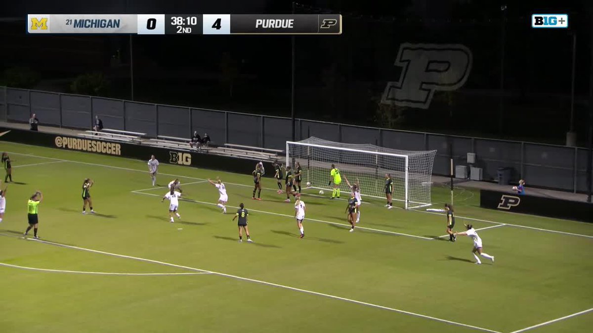 Michigan players celebrate after scoring against Purdue during a Big Ten women's soccer match, with the scoreboard showing Michigan at 0 and Purdue at 4, with 38:10 remaining in the 2nd half. The image captures the moment following the Wolverines' set-piece goal that got them on the board, as referenced in the caption about "set piece perfection" from @umichwsoccer.
