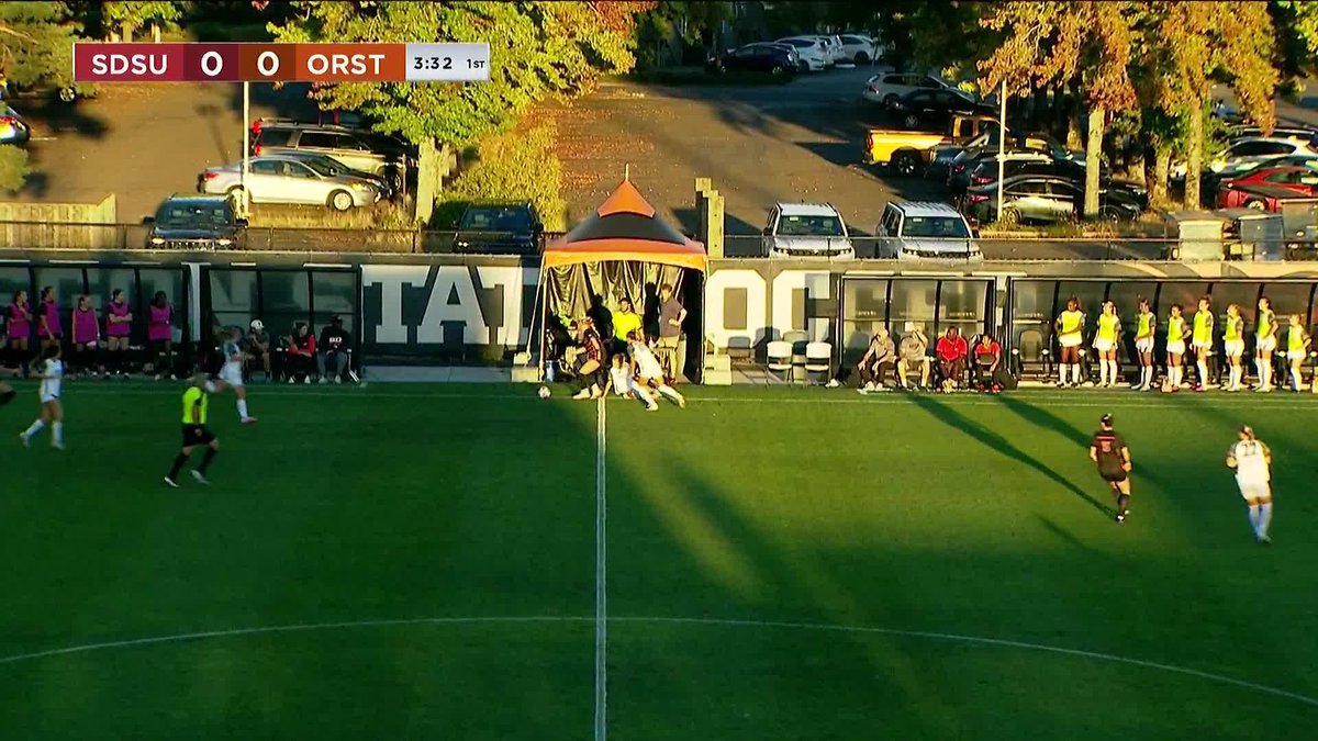A screenshot of a women's soccer match between SDSU and ORST, tied 0-0 with 3:32 left in the 1st half, showing players on the field and a parking lot in the background.