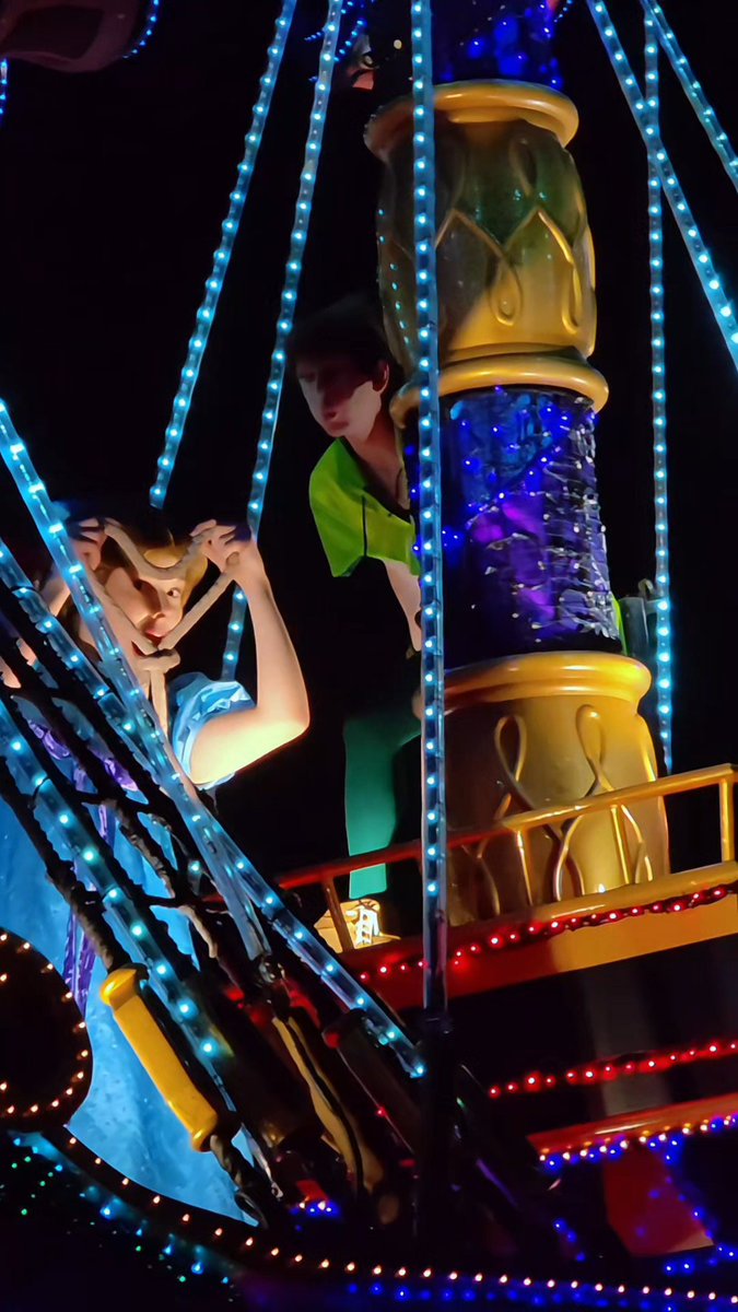 A nighttime parade float features a large animated figure of Peter Pan holding Wendy, illuminated by sparkling blue and red lights against the dark sky. The whimsical, Disney-themed display perfectly matches the caption's excited reaction, capturing the magical moment of spotting beloved characters up close.