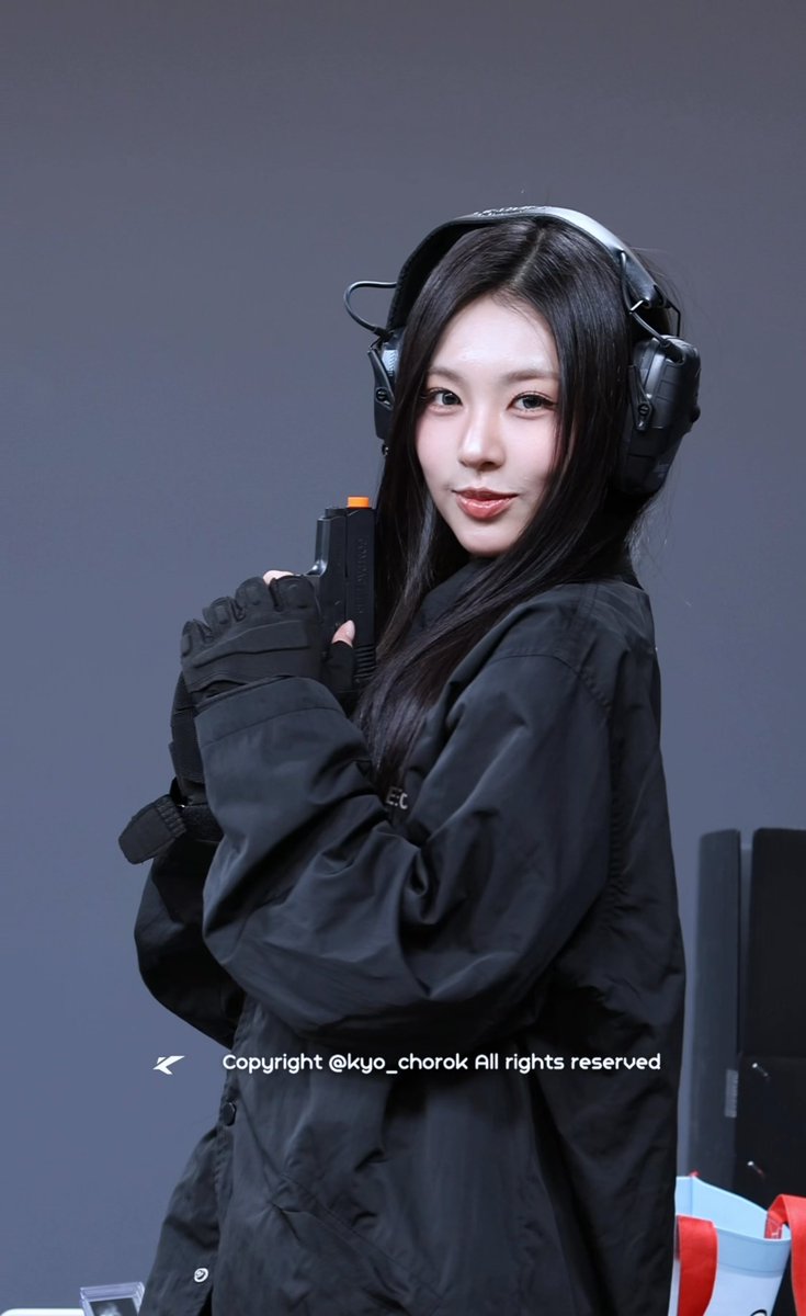 A woman with long dark hair wearing tactical gear including black headphones, gloves, and a black jacket holds what appears to be a prop weapon, with text 'Copyright @kyo_chorok All rights reserved' visible.