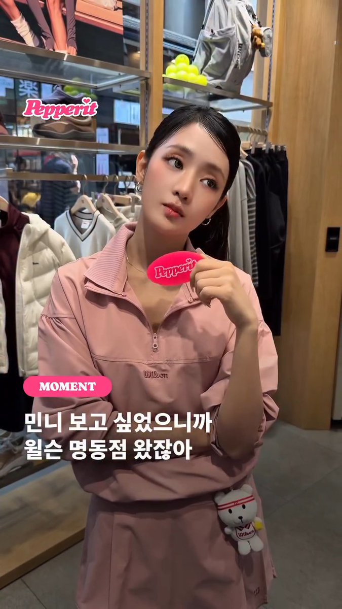 A young woman wearing a pink Wilson tracksuit poses in what appears to be a clothing store, with a pink 'Pepperit' speech bubble near her head. Overlaid text reads 'MOMENT' and Korean text '민니 보고 싶었으니까 월슨 명동점 왔잖아' (I missed Minni so I came to the Wilson Myeongdong store).