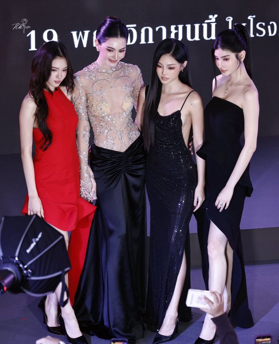 Four Thai celebrities posing together at a formal event, wearing elegant evening gowns in red, black/silver, black sequin, and black one-shoulder designs.