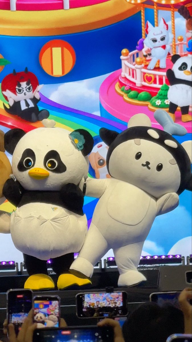 Two large mascot costumes—one resembling a panda with yellow shoes and another resembling a rabbit-like character in a hood—perform on stage at what appears to be a Chiikawa character event, with audience members filming on phones.