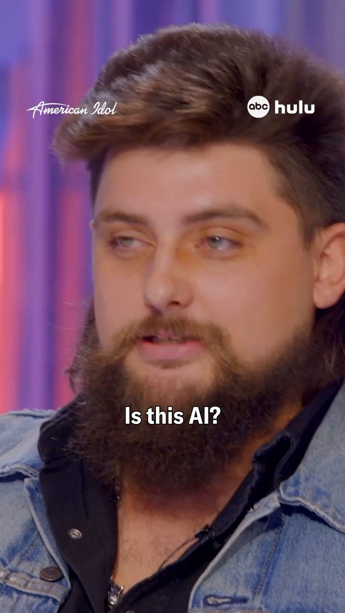 A close-up of a bearded man with brown hair on American Idol (ABC/Hulu), with text overlay reading 'Is this AI?' suggesting a meme or commentary about the contestant.