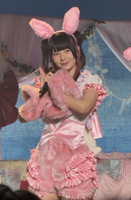 A young woman in a pink frilly costume with bunny ears performing on stage while holding a microphone.