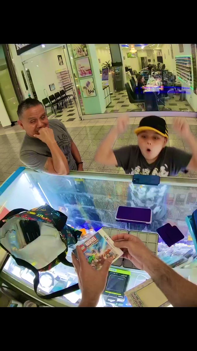 A person holds a 60-card "Miracle" booster pack above a glass display case while an excited boy in a baseball cap throws his arms up in surprise and an amused man covers his mouth watching the moment unfold inside what appears to be a card shop. The scene captures the dramatic reveal suggested by the post, showing the "miracle" item being presented as the unexpected solution to fixing the boy's broken DS.