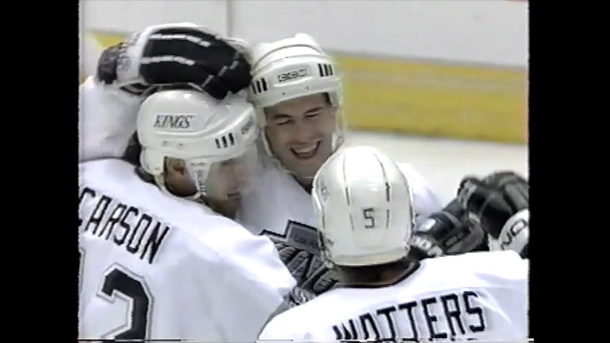 Los Angeles Kings hockey players in white jerseys, including one named 'CARSON' (#2) and another with 'WOTTERS' on the back, celebrate together with helmets and gloves on the ice.