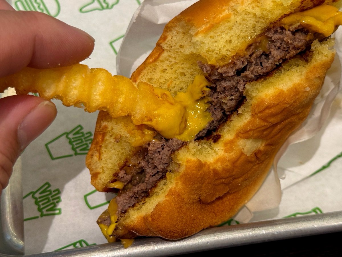 h_gashiyama's tweet photo. アメリカに1年住んでいた経験から言わせてもらうとだな、SHAKE SHACKの、

ハンバーガー
野菜抜き
チーズトッピング

これがアメリカ現地のハンバーガーに1番近いと思う

それはなぜか？

日本の野菜は、アメリカの野菜に比べて、『味が薄い＆水分が多い』
全部の野菜がそうじゃないけど、特に玉ねぎ＆トマトはそう

それは日本の野菜の長所でもあり、和食に向いているポイントでもあるのだが、ことバーガーにおいては雰囲気が変わる

ちょっともったいない気もするが、思い切って、野菜を抜いた、シンプルなバーガーを食べてみてほしい

そうすると、
『こんなに肉の味が濃いのか！』
『パン生地ってこんなに甘いの！？』
『口溶けの一体感がすごい！』

って感想になると思う！
野菜の水分で味が薄まらない分、バーガーの輪郭をよりはっきり味わえる！

特にSHAKE SHACKはバンズがすごい
断面を見たら分かる通り＂黄色い＂のだ

これは、＂卵黄を多く使った、リッチなブリオッシュ生地＂である証拠
味としては、甘みが強く、口溶けが良い

ゆえに、ジューシーなパティとの相性が素晴らしい！！
『飲める』テクスチャーになる

さらに食べ方としてオススメなのが、味変として、ポテトを筆のように使って、マスタードをちょんちょん塗って食べる

こうすると、マスタードの味に支配されすぎない＂パティとマスタードの黄金比率＂で味変が楽しめる！

SHAKE SHACKへ対する価値観がガラッと変わると思うので、ぜひ試してほしい！