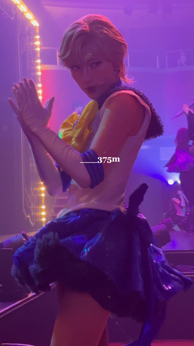 A blonde cosplayer dressed as Sailor Uranus performs on a purple-lit stage, with text overlay reading '____375m'.