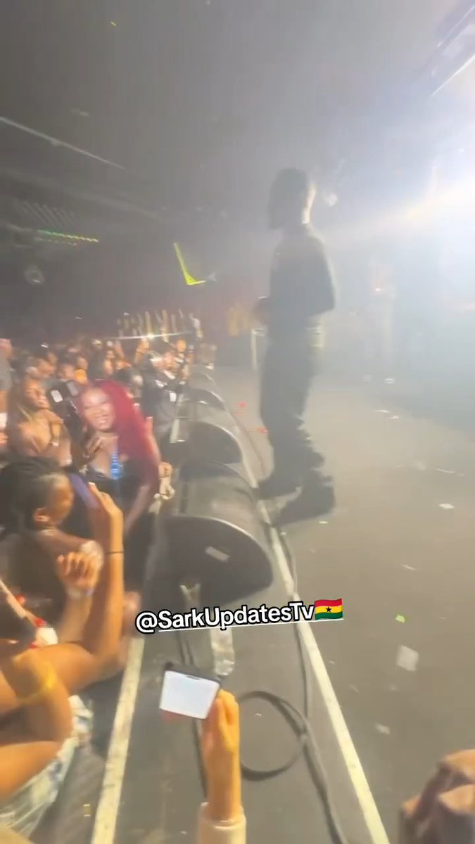 A hazy, low-quality concert photograph with the watermark "@SarkUpdatesTv" showing a performer on stage and an enthusiastic crowd with red hair in the front row, likely from a Sarkodie event in Ghana.