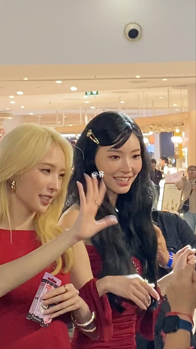 Two women, one with blonde hair and one with dark hair, smile and pose together indoors, with the text "@予" visible between them.