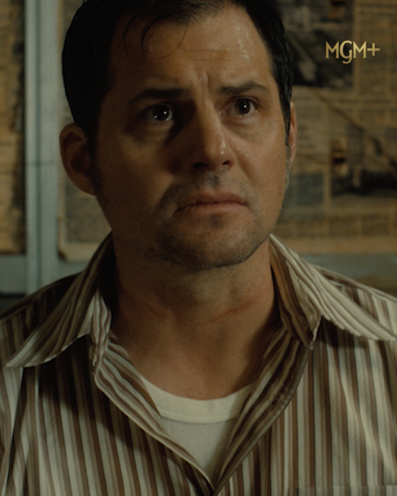 A close-up shot from a TV show featuring a man in a striped shirt with a serious expression, with an 'MGM+' logo in the top right corner.