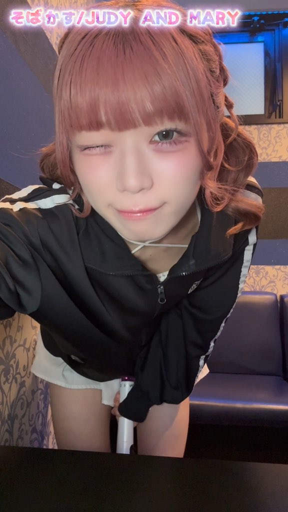 Close-up selfie of a person with reddish-brown hair and bangs, winking at the camera, wearing a black track jacket over a white top, with the text 'そばかす/JUDY AND MARY' overlaid at the top.