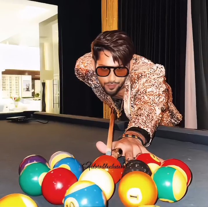 A man wearing orange-tinted sunglasses and a leopard-print jacket plays pool, leaning over a table and aiming his cue stick at a rack of colorful billiard balls, with "CelebWithSweet" watermarked on the image.