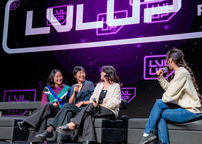 Four women sitting on a couch on stage at a 'LVL UP' esports event, holding microphones and engaged in a panel discussion.