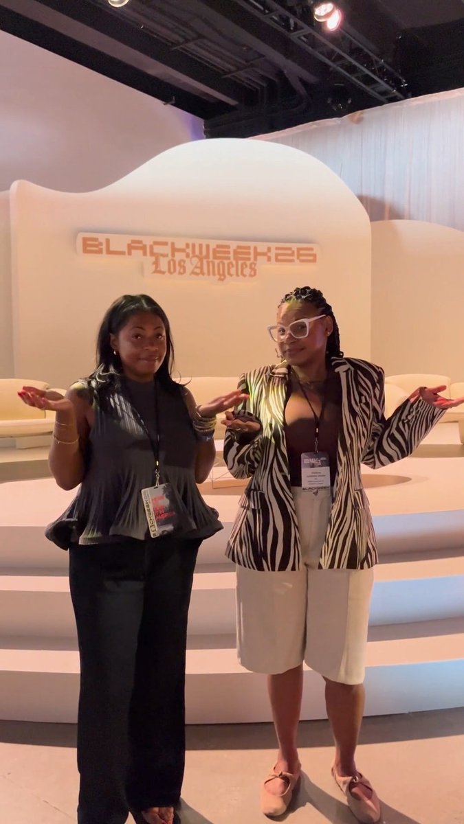 Two members of the VML Inclusion & Impact team pose with open arms at the "BLACKWEEK 25 Los Angeles" conference, wearing event lanyards and showcasing bold, expressive style against the branded backdrop.