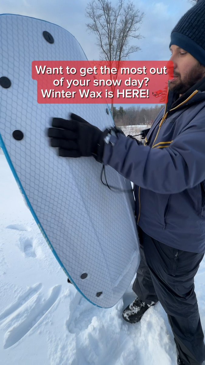 A man in winter clothing holding a white snow/surf board in a snowy outdoor setting, with text overlay: 'Want to get the most out of your snow day? Winter Wax is HERE!'