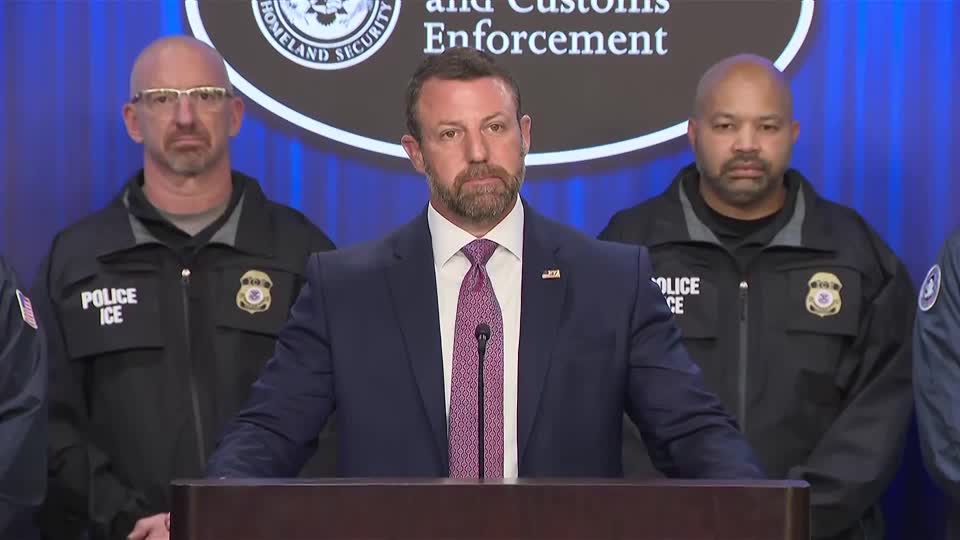 Homeland Security Secretary Markwayne Mullin speaks at a podium bearing the ICE (Immigration and Customs Enforcement) seal, flanked by uniformed ICE police officers, while addressing the media about the agency's policy implications following the shooting of Oscar Belgal in New York.