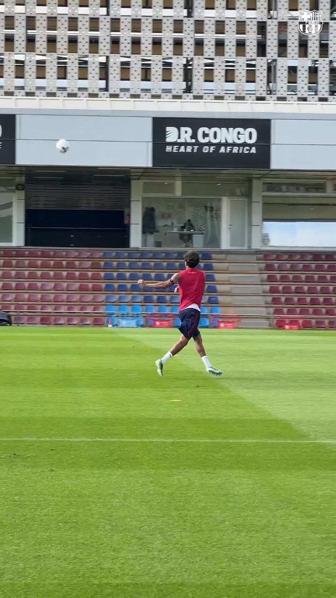 A football player in a red training shirt kicks a ball across an empty stadium pitch, with a "D.R. CONGO - HEART OF AFRICA" advertising banner visible on the stands behind him.