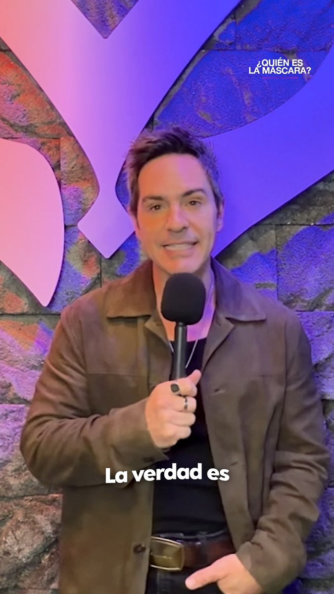 A man in a brown jacket holds a microphone in front of a purple backdrop with the text "¿QUIÉN ES LA MÁSCARA?" and "La verdad es" on screen.