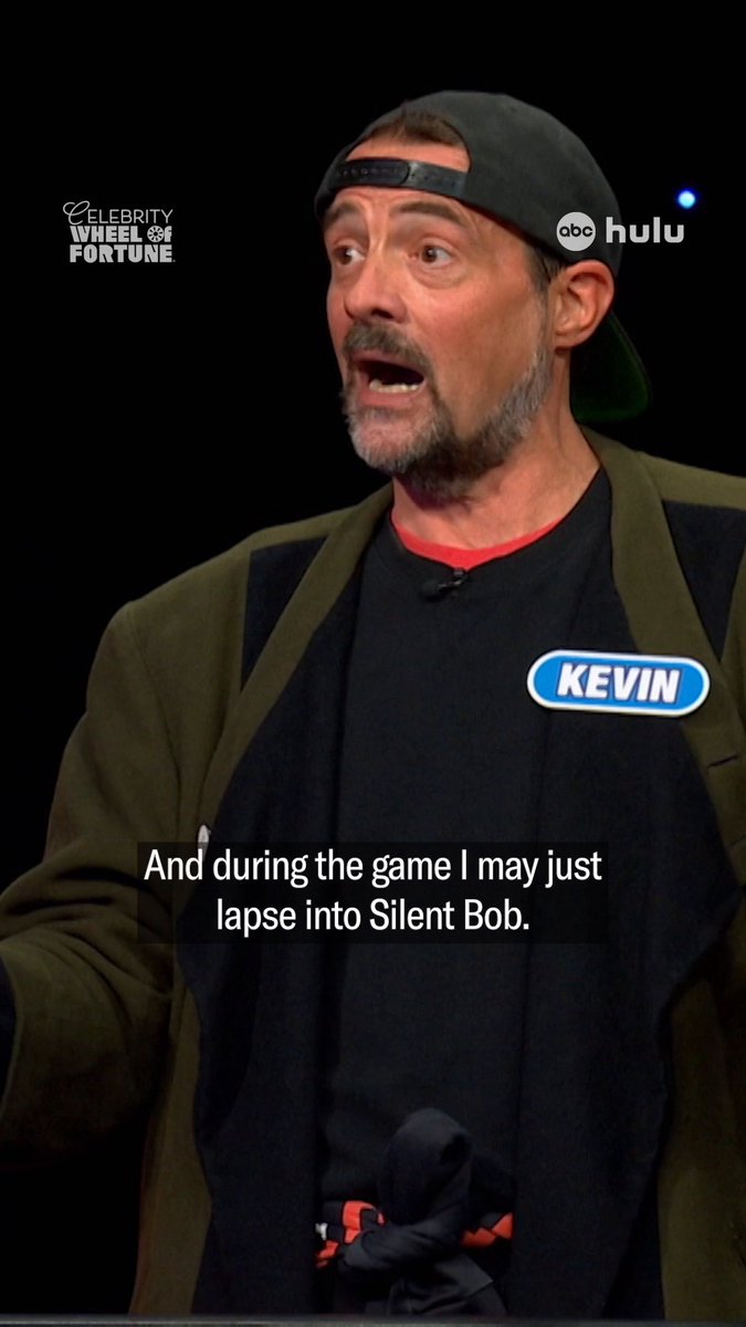 Screenshot from Celebrity Wheel of Fortune on ABC/Hulu featuring Kevin Smith, wearing a 'KEVIN' name tag, with the subtitle 'And during the game I may just lapse into Silent Bob.'