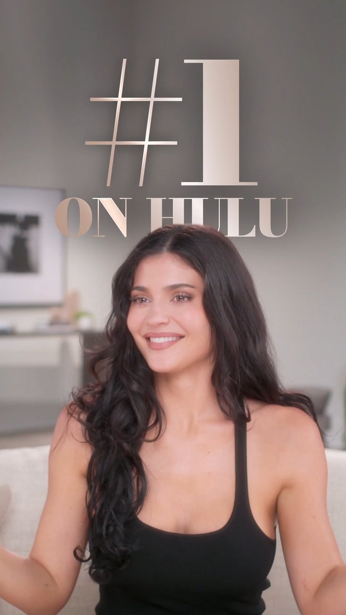 The image shows a smiling woman with long dark wavy hair wearing a black tank top, seated in a bright room with a "#1 ON HULU" graphic overlay above her. This promotional image celebrates the news shared in the post that The Kardashians season 8 is the #1 show on Hulu.