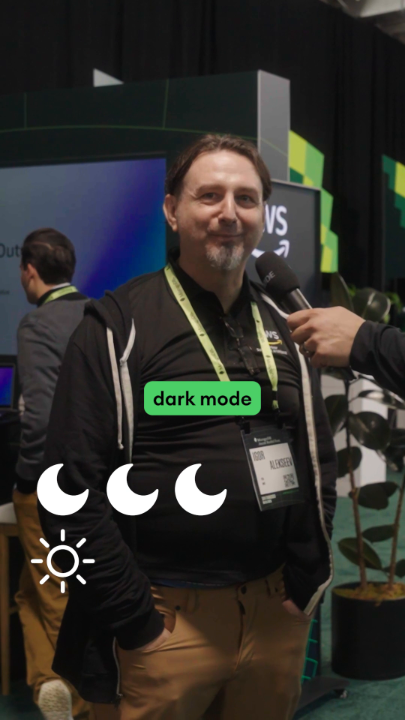 A man with a beard is being interviewed at what appears to be a tech conference, with a 'dark mode' graphic and crescent moon icons overlaid on the image.