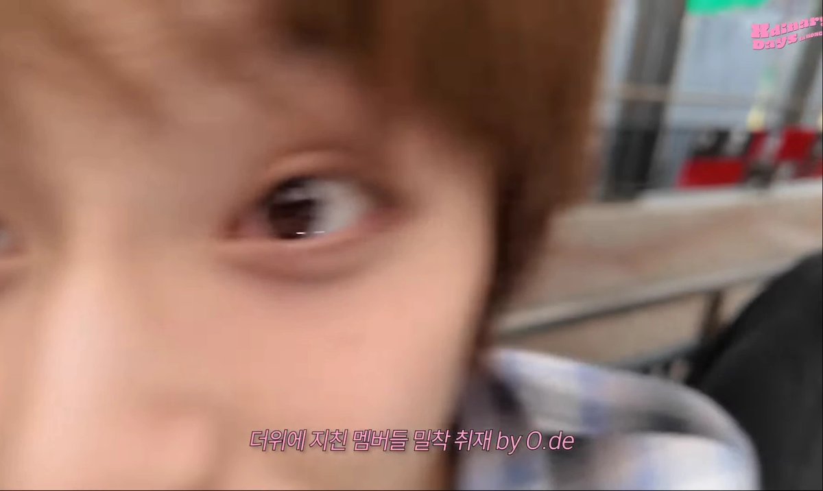 Close-up blurry shot of a person's eye with Korean text overlay reading '다위에 지친 멤버들 밀착 취재 by O.de' (Close coverage of exhausted Da-woo members by O.de).