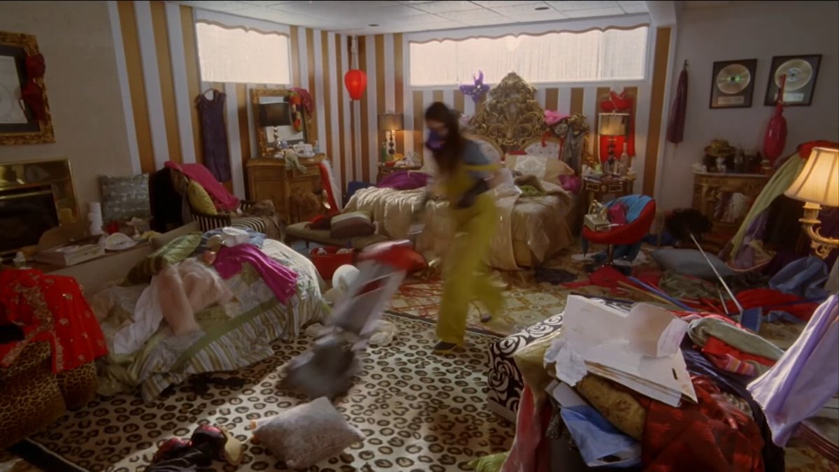 A girl in a yellow dress spins in a chaotic, clothing-strewn bedroom with an ornate gold bed and striped walls, capturing a moment of playful disarray. The scene reflects the fun, entertaining spirit of the movie "La nueva cenicienta 2," being promoted for a Friday popcorn movie showing on channel El5.