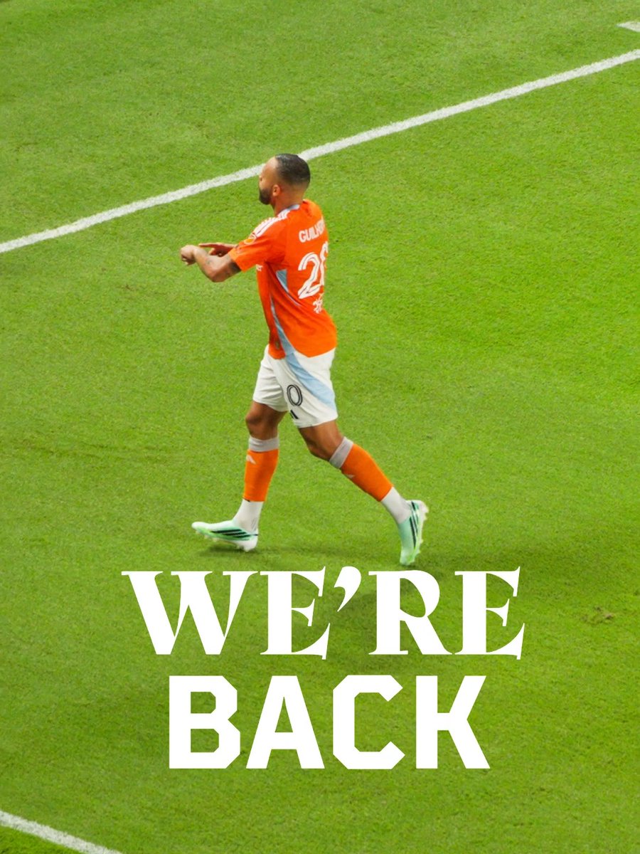 A soccer player wearing an orange jersey with the number 25 and the name 'GUL...', running on a green field, with large white text reading 'WE'RE BACK' overlaid at the bottom.