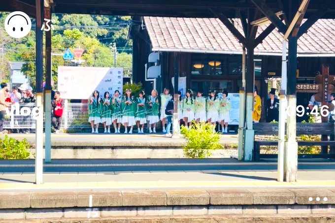 A photo taken from a train platform showing a group of schoolgirls in green uniforms waving, with a timestamp of 9:46 visible on the image.