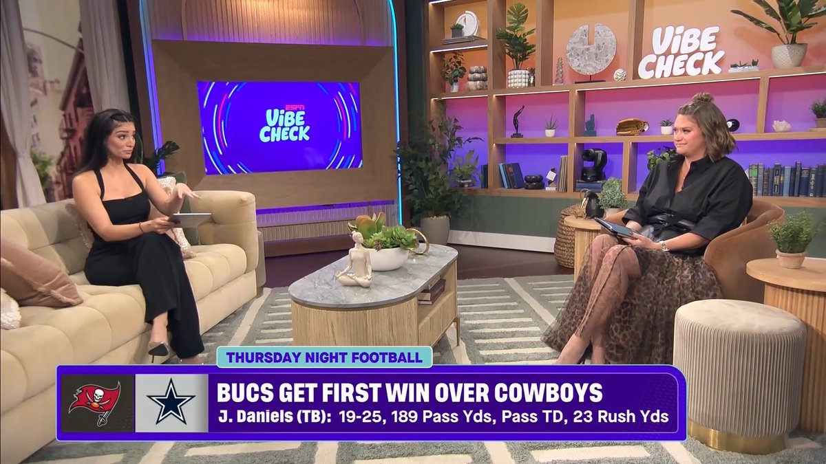 Two female hosts sit across from each other on a brightly lit ESPN "Vibe Check" talk show set, discussing Thursday Night Football where the Buccaneers secured their first win over the Cowboys, highlighted by J. Daniels' stat line of 19-25, 189 pass yards, a passing TD, and 23 rush yards, as displayed in the lower-third graphic.
