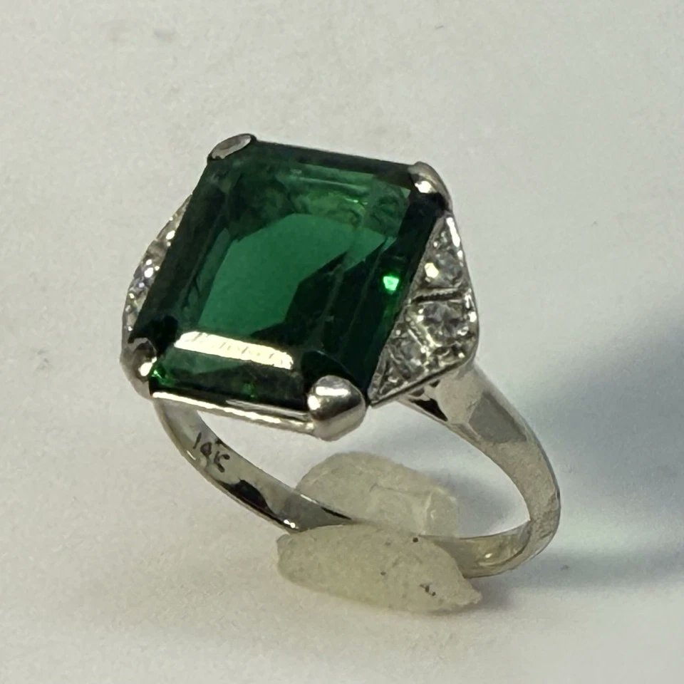 Nobel_Antiques's tweet photo. -Stunning Antique American Art Deco Ring- 
Handcrafted in white gold with a striking emerald-cut laboratory made green stone and six natural diamonds.
Regarding the use of synthetic stones in Art Deco period:
During the Art Deco era of the 1920s and 1930s, the use of synthetic gemstones in jewelry was not inherently intended to deceive consumers with imitation or “fake” stones. Rather, it reflected the emergence of groundbreaking laboratory technology that, for the first time in history, made vibrant colored gemstones more widely available and affordable. Synthetic sapphires, rubies, spinels, and other lab-created stones became popular because they offered jewelers exciting new design possibilities at a time when bold geometric patterns and vivid color contrasts defined the Art Deco aesthetic. These stones were often viewed as modern scientific achievements and allowed designers to create striking jewelry that might otherwise have been prohibitively expensive. While proper representation and disclosure still mattered, the presence of synthetic stones in many period pieces should be understood within the historical context of innovation and evolving jewelry manufacturing rather than automatically assuming an intent to mislead
#ArtDeco #VintageJewelry #AntiqueJewelry #EstateJewelry #WhiteGold #DiamondRing #DecoStyle #VintageRing