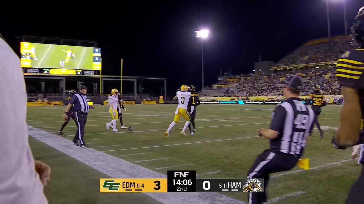 A CFL football game featuring the Edmonton Elks leading the Hamilton Tiger-Cats 3-0 in the 2nd quarter with 14:06 remaining, captured just as a player makes a play downfield under the stadium lights in front of a packed crowd. The image corresponds with a highlight of Austin Mack's spectacular catch, showcasing the offensive action from Hamilton's possession.