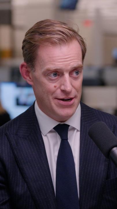 A man in a pinstripe suit and dark tie speaks into a microphone in what appears to be an office or broadcast setting, likely captured during an interview about hedge funds and higher interest rates. The image relates to the post featuring Mark Wilson of Goldman Sachs discussing how hedge funds are navigating the current interest rate environment on "The Markets."